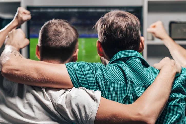 amigos se abraçam ao ver jogo de futebol pela televisão